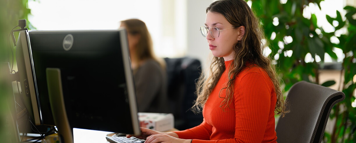 A woman is sitting at a desk and typing something on the keyboard.